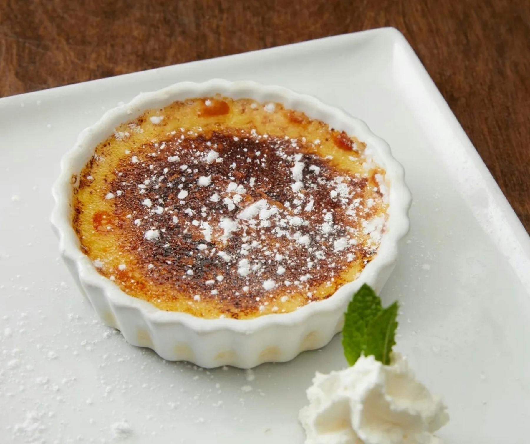 A close-up image of a crème brûlée dessert, showcasing its golden and crackled sugar on top.