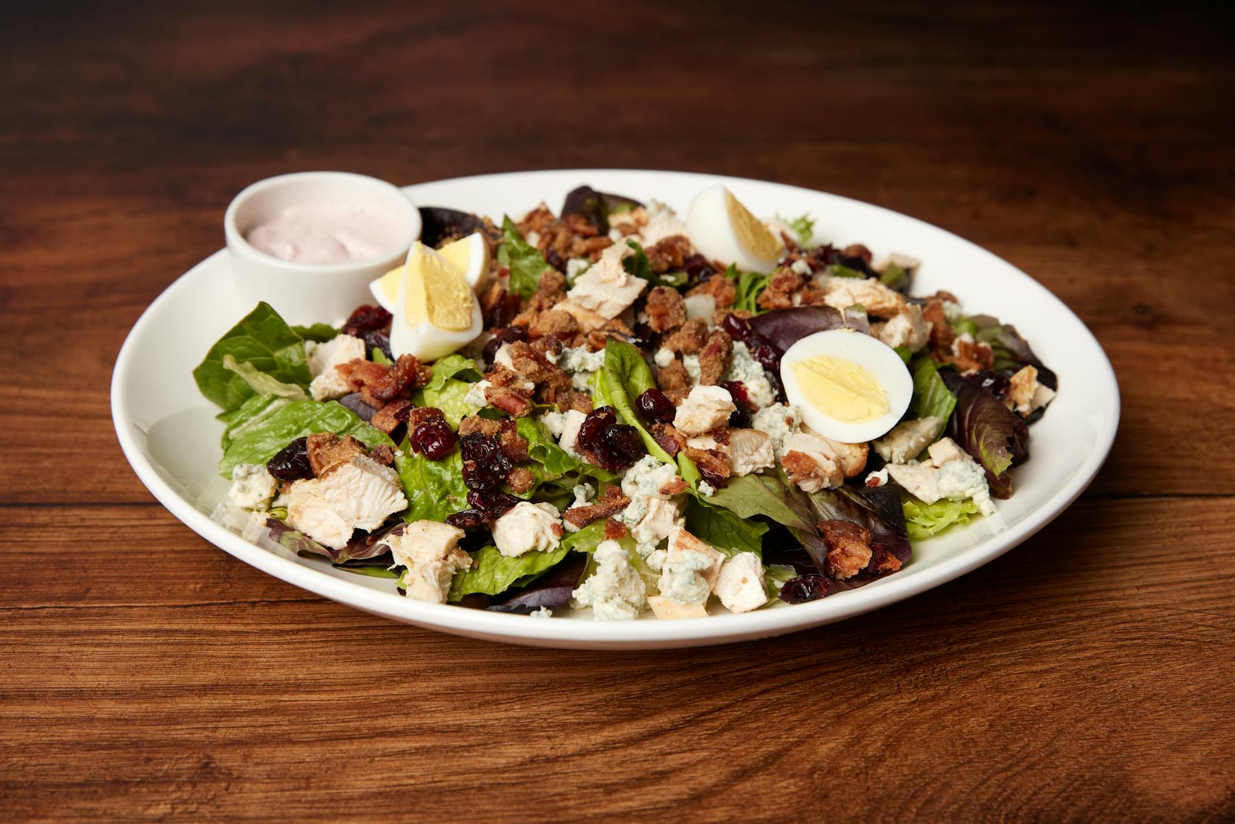 A salad featuring mixed greens, topped with sliced grilled chicken, pecans, dried cranberries, and crumbled bleu cheese.