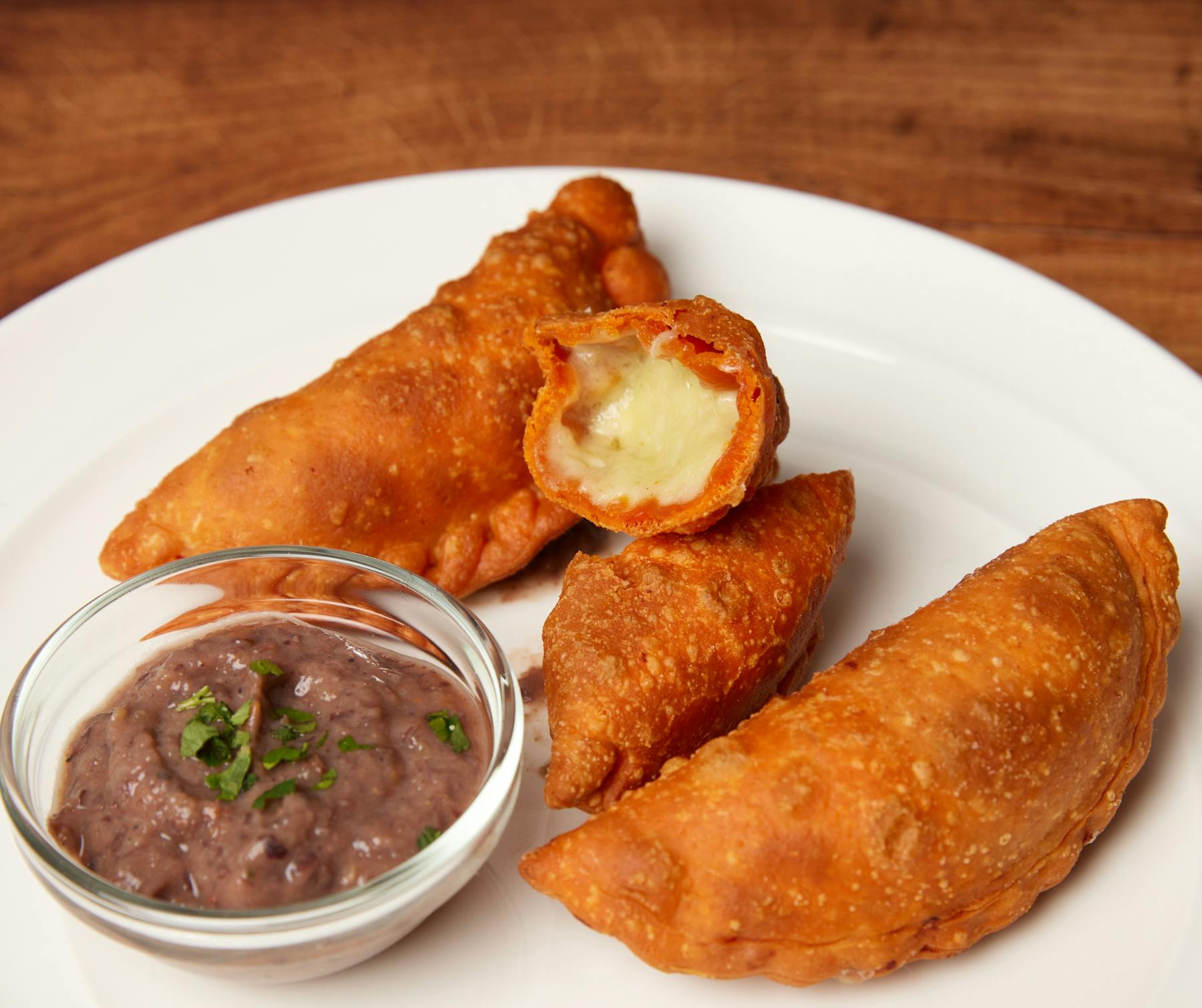 Fried empanadas with queso filling, served with herb-garnished dipping sauce.