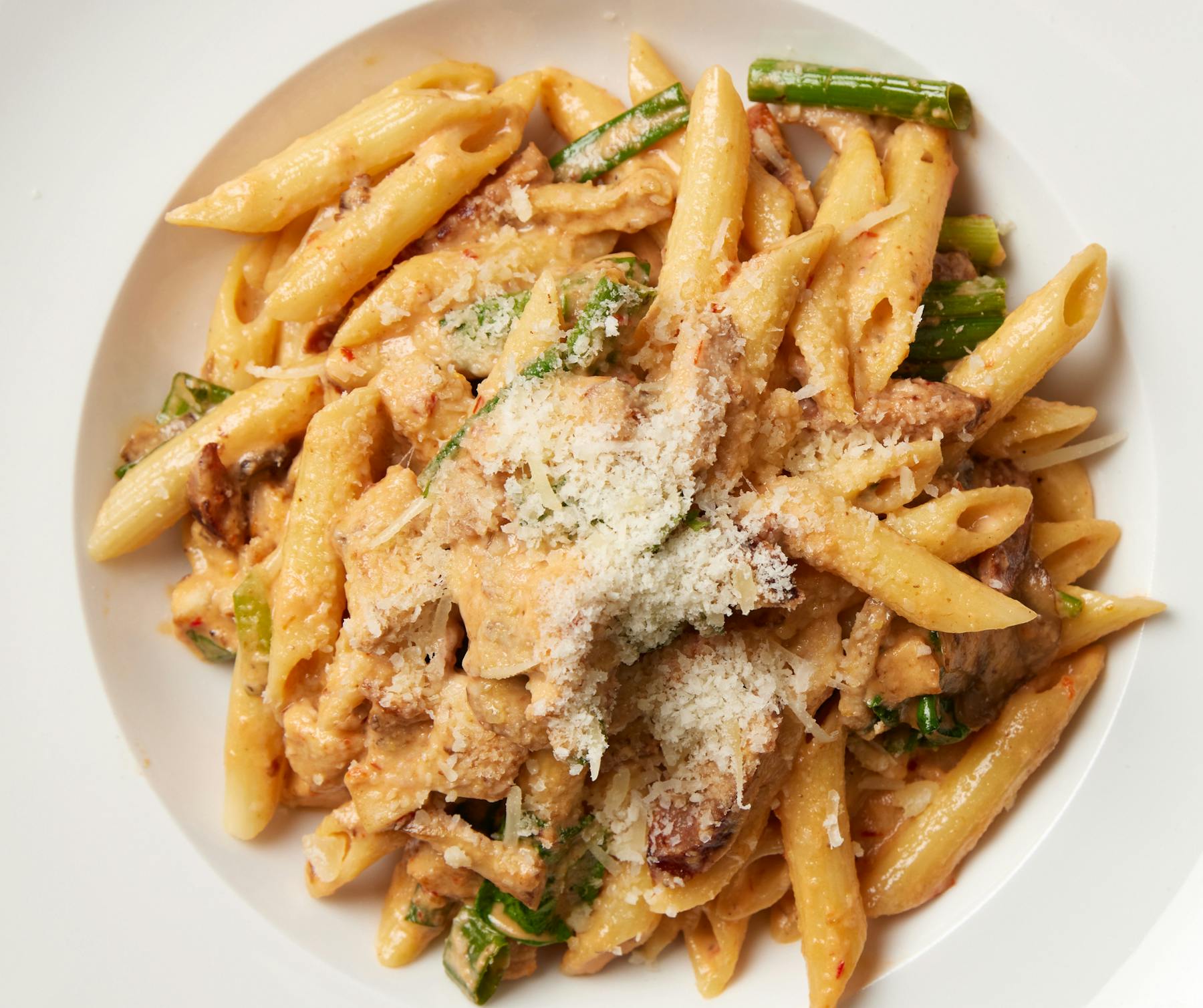  Creamy penne pasta with chicken, sausage, shrimp, and vegetables on a white plate.