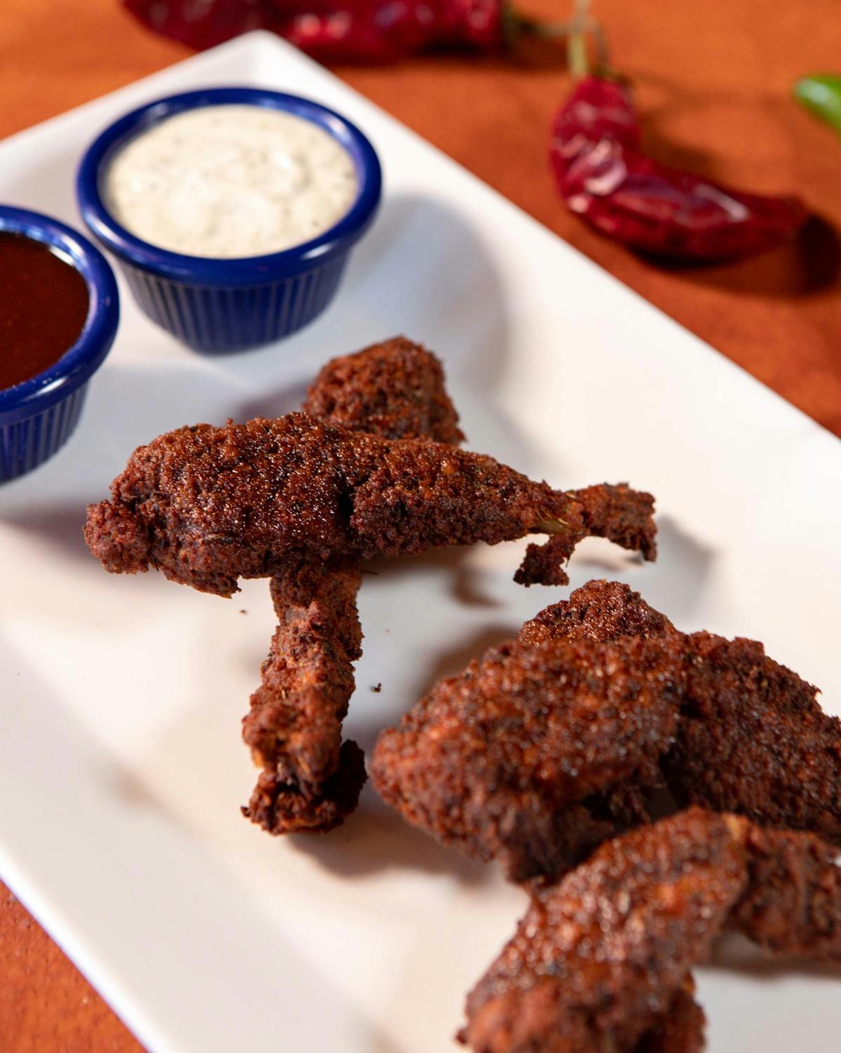 5 frog legs stacked on a plate with dipping sauces