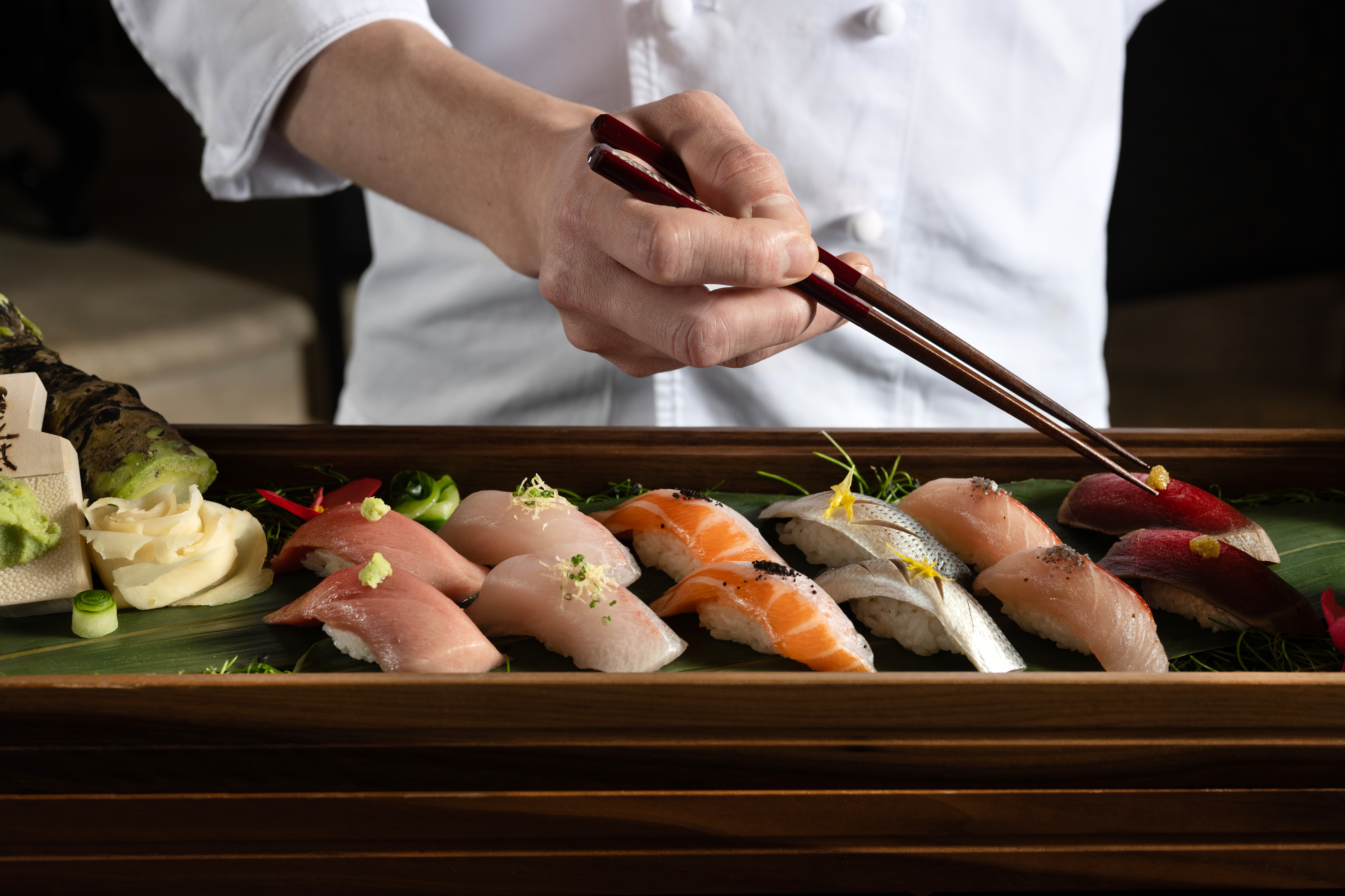 a person holding chopsticks to a plate of sushi