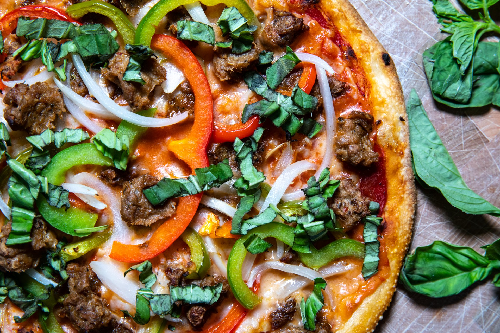 A delicious pizza topped with meat, peppers, and onions, displayed on a rustic wooden cutting board