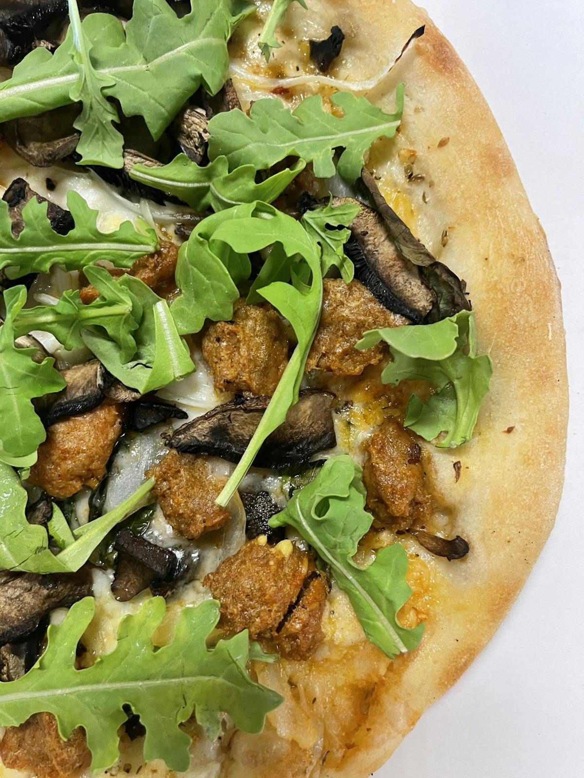 A white plate holds a pizza topped with mushrooms and fresh greens, showcasing a delicious and vibrant meal