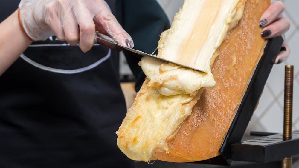 a hand holding a fork and knife on a cutting board with a cake