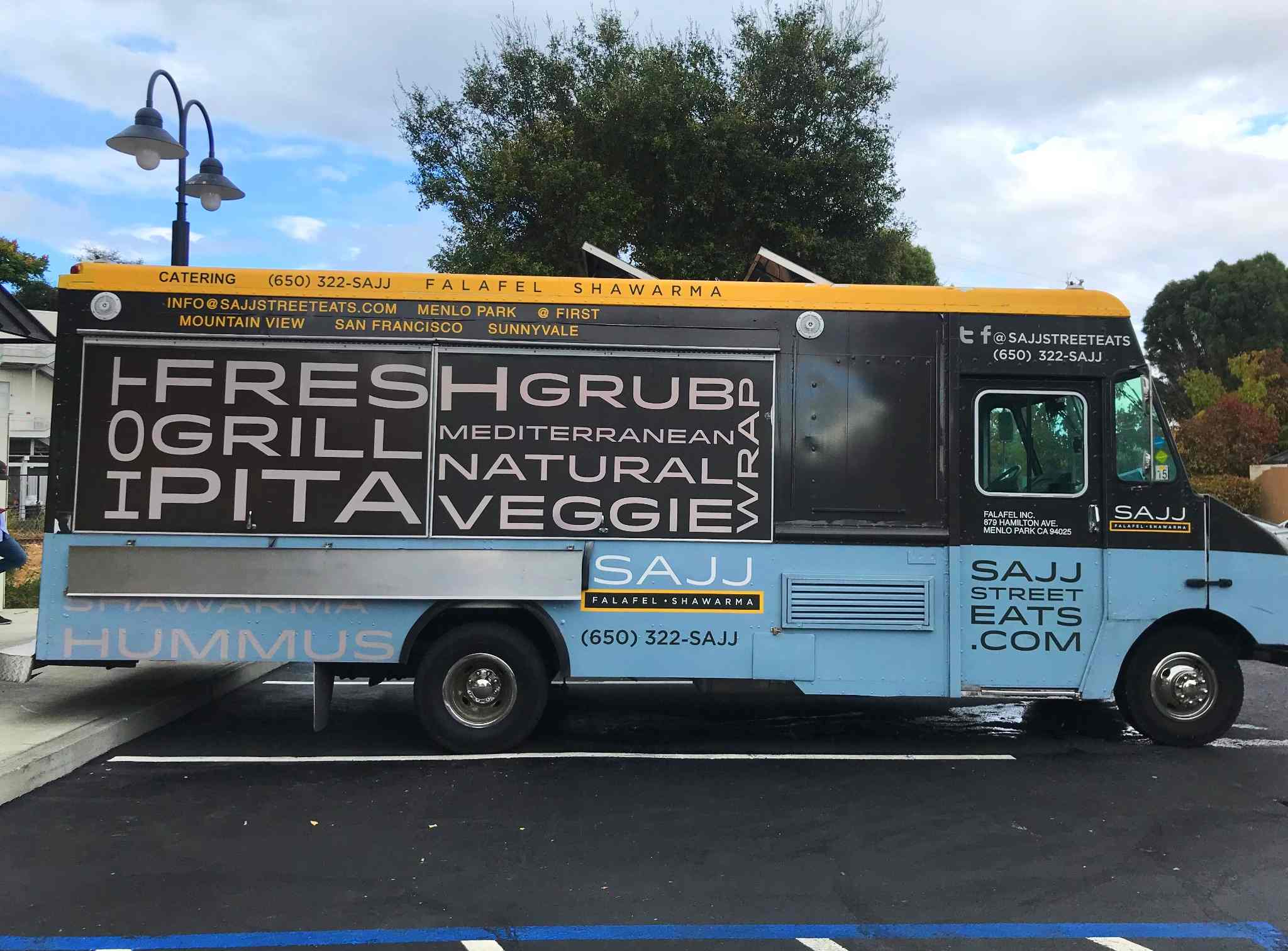 Blue and yellow Sajj food truck with bold text advertising Mediterranean dishes.