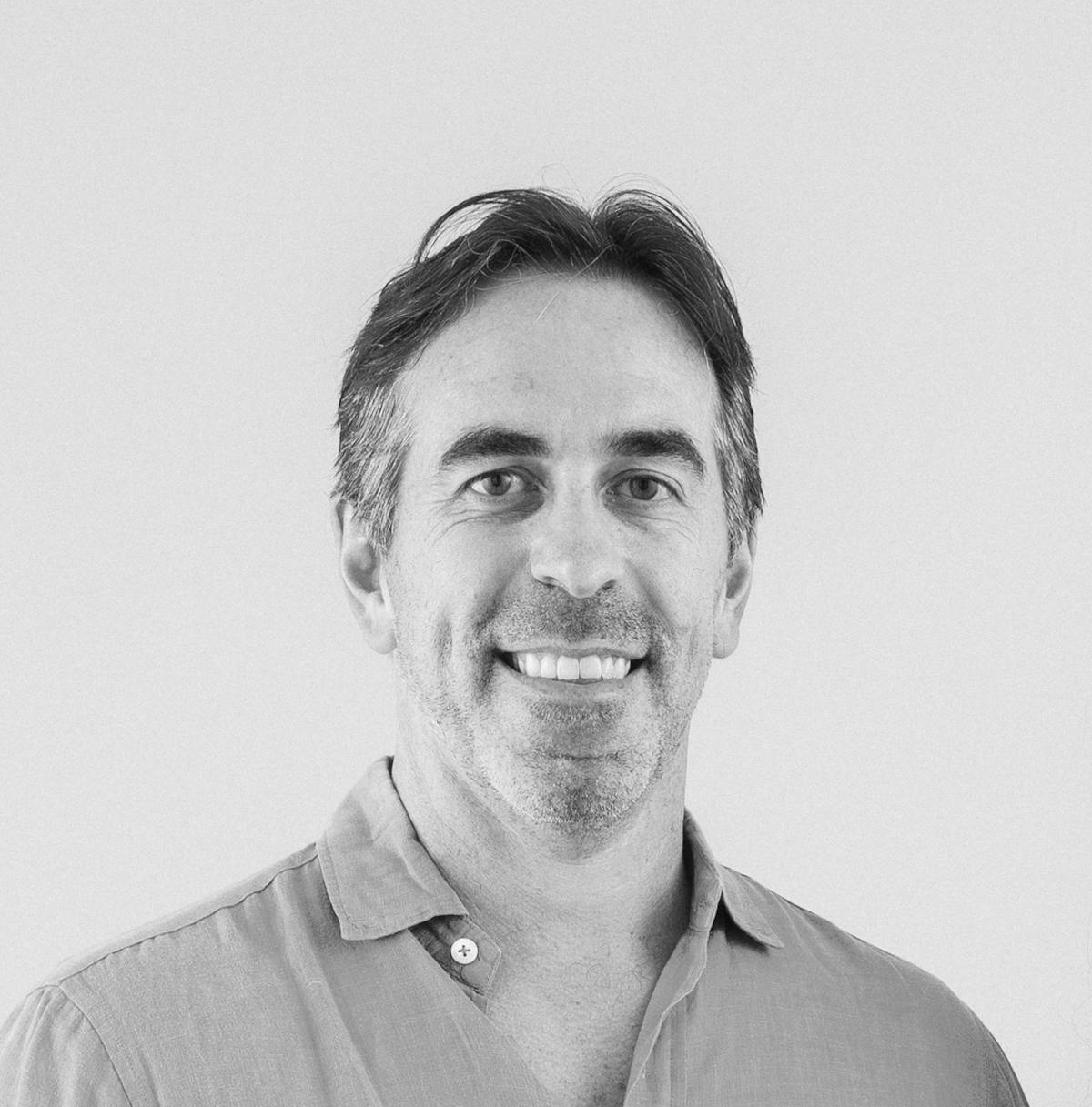 A smiling man with a collared shirt poses for the camera in a black and white headshot photo.