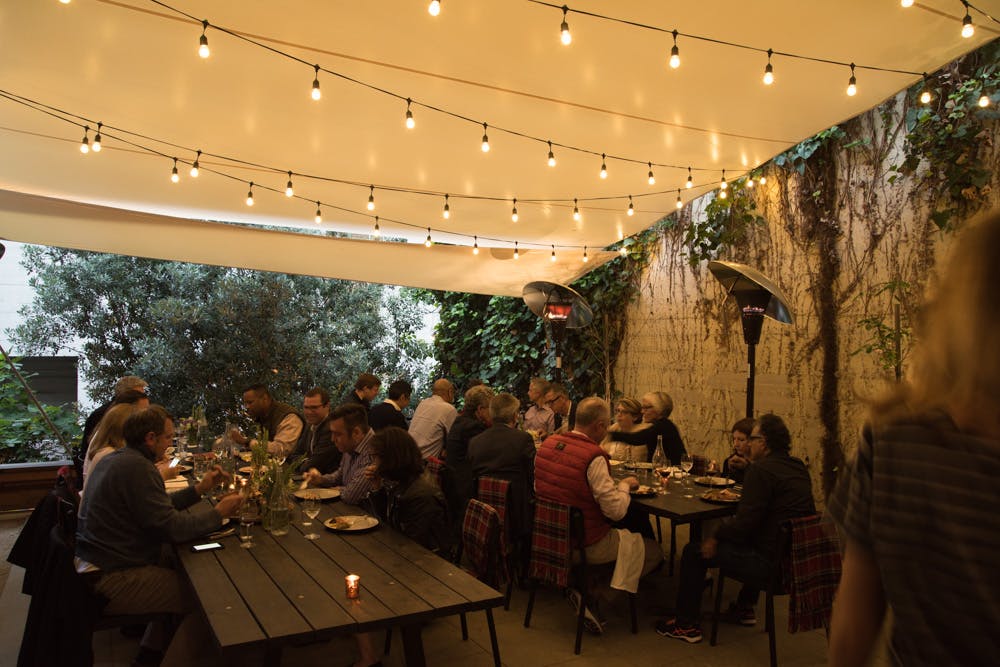 large tables set in the garden decorated with light bulbs on the ceiling with people seated on the table