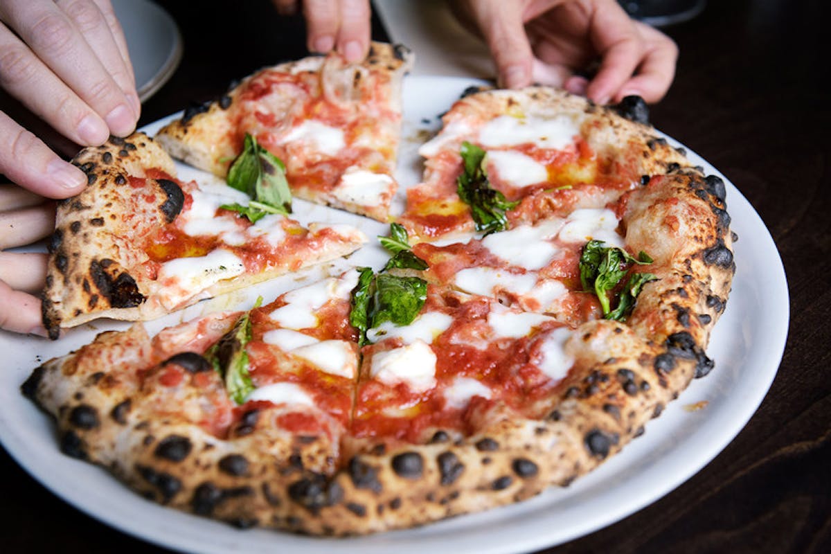 a pizza on a table with someone picking a slice 