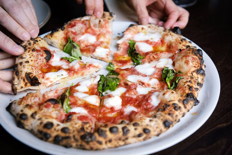 a pizza on a table with someone picking a slice