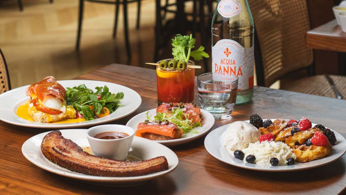 A beautifully plated spread of gourmet dishes, including thick-cut bacon, smoked salmon, and fresh berry waffles, highlighting the elevated culinary experience at Sofia Fine Dining Italian Steakhouse.