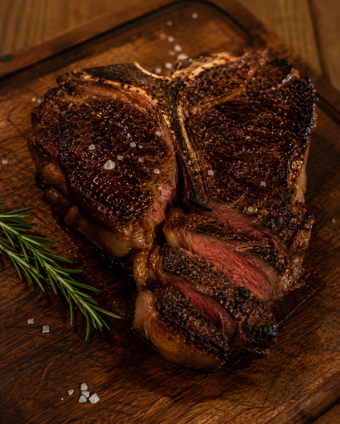 Dry-aged porterhouse steak on a wooden cutting board with coarse salt and fresh rosemary