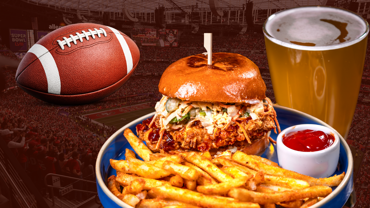Fried chicken sandwich with fries and ketchup beside a beer, set against a football stadium backdrop.