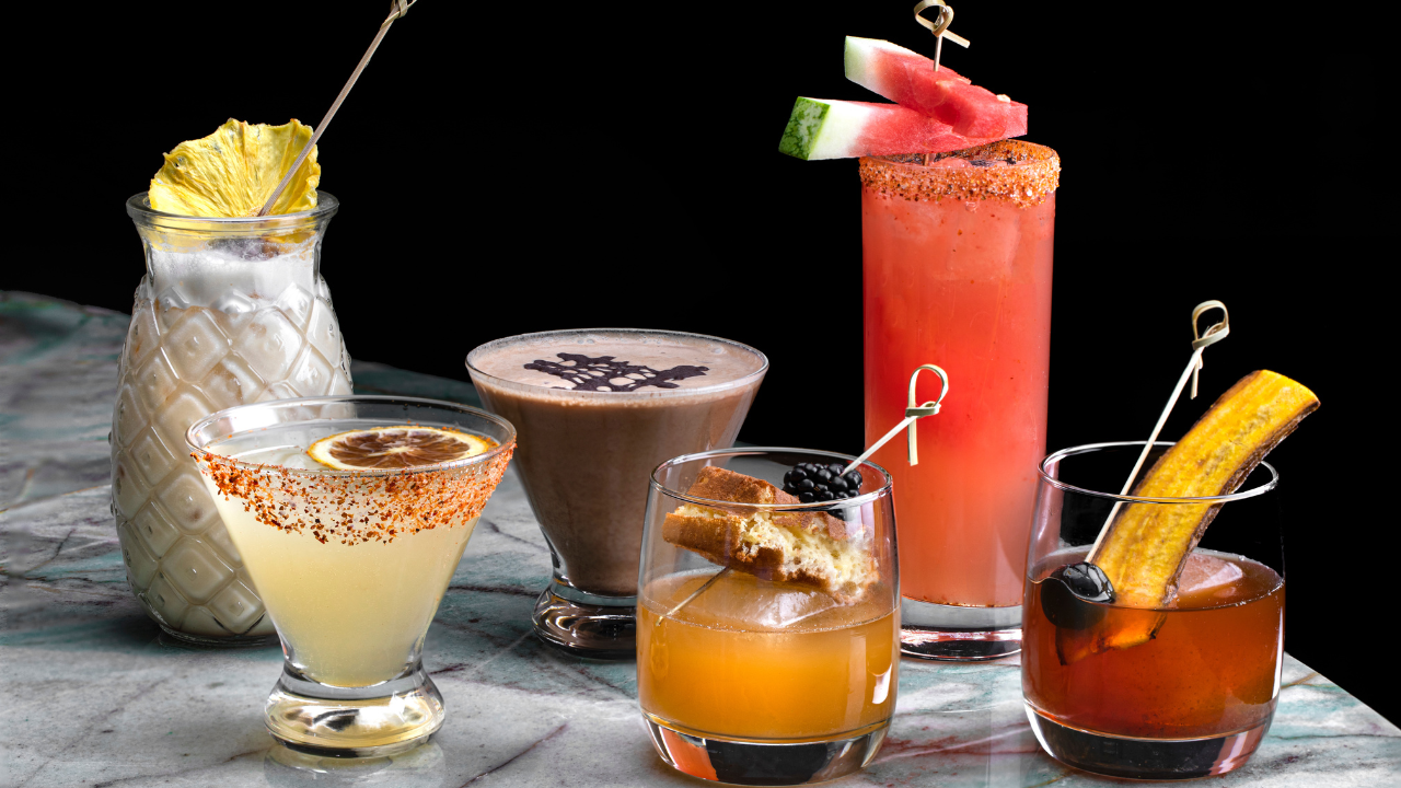 Assorted craft cocktails with garnishes arranged on a marble surface against a black background.
