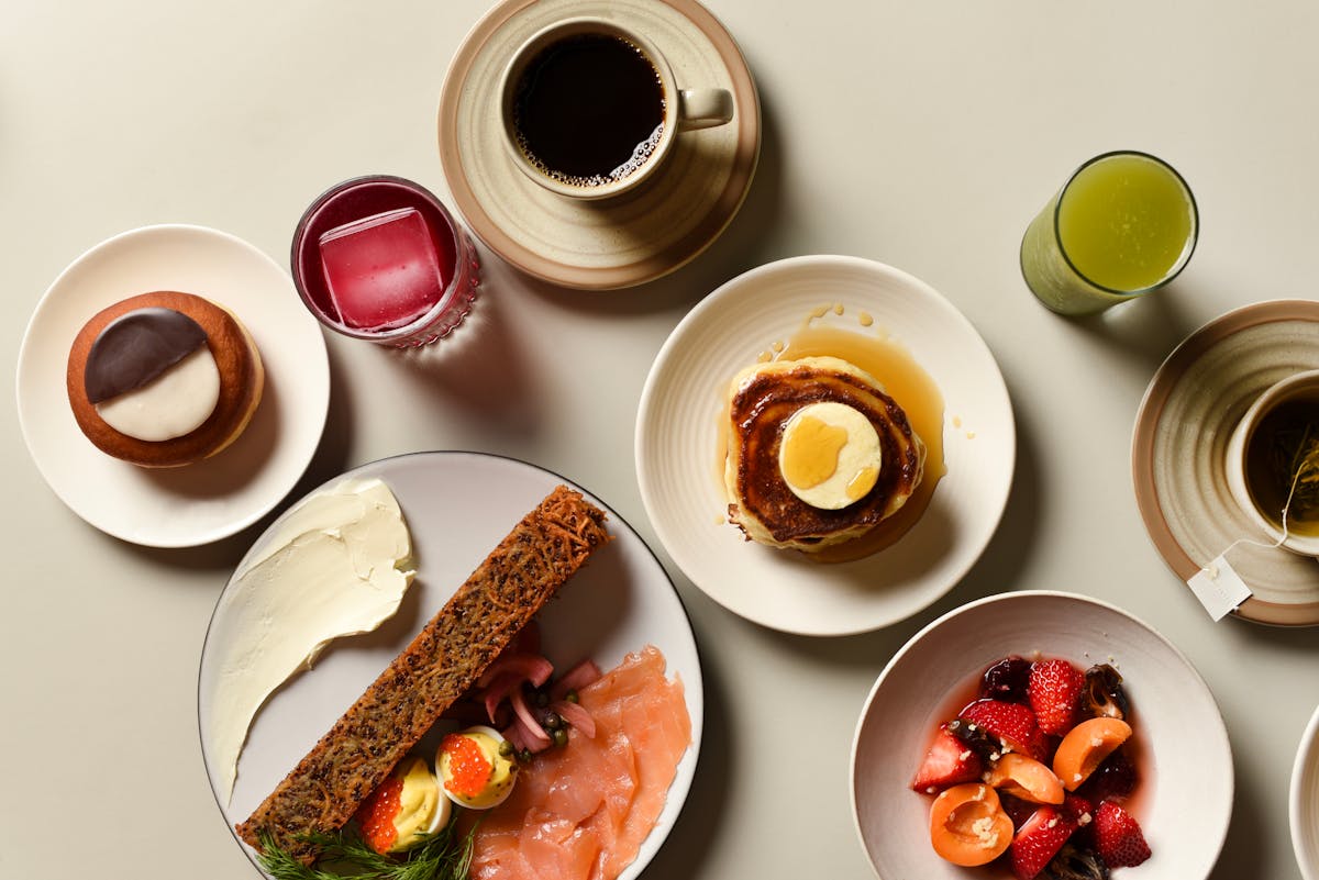 assorted breakfast plates on table, pancakes, fruit, and smoked salmon