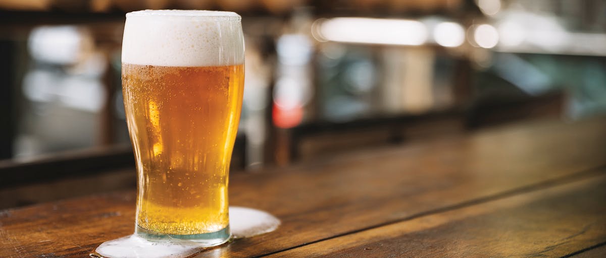 a close up of a glass cup on a wooden table and a beer