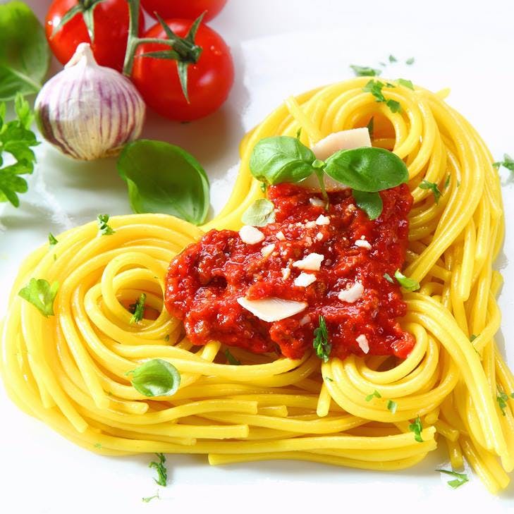 a closeup of a plate filled with pasta on a heart-shaped form next to some veggies