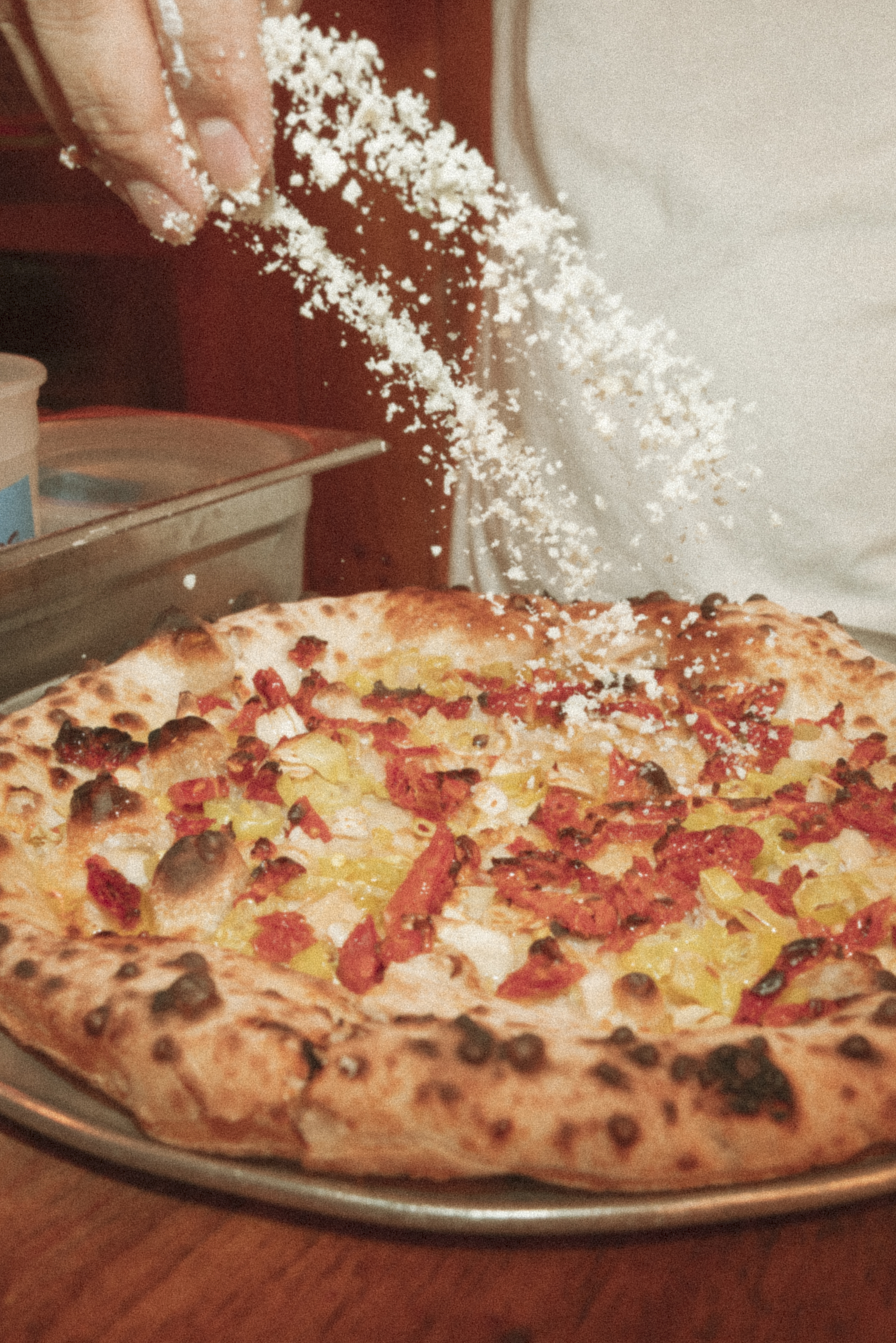 a person sprinkling cheese on a pizza