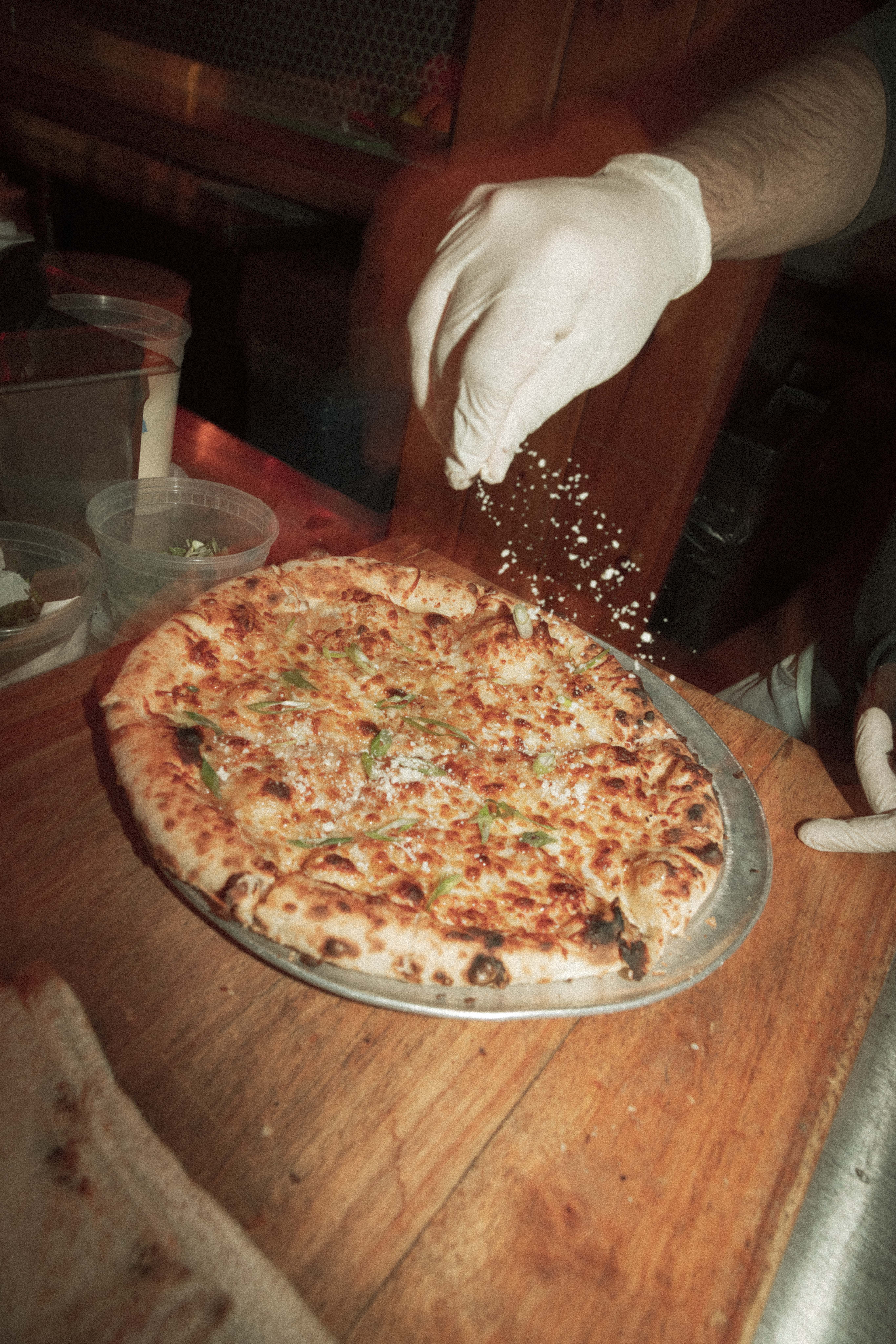 a person sprinkling cheese on a pizza