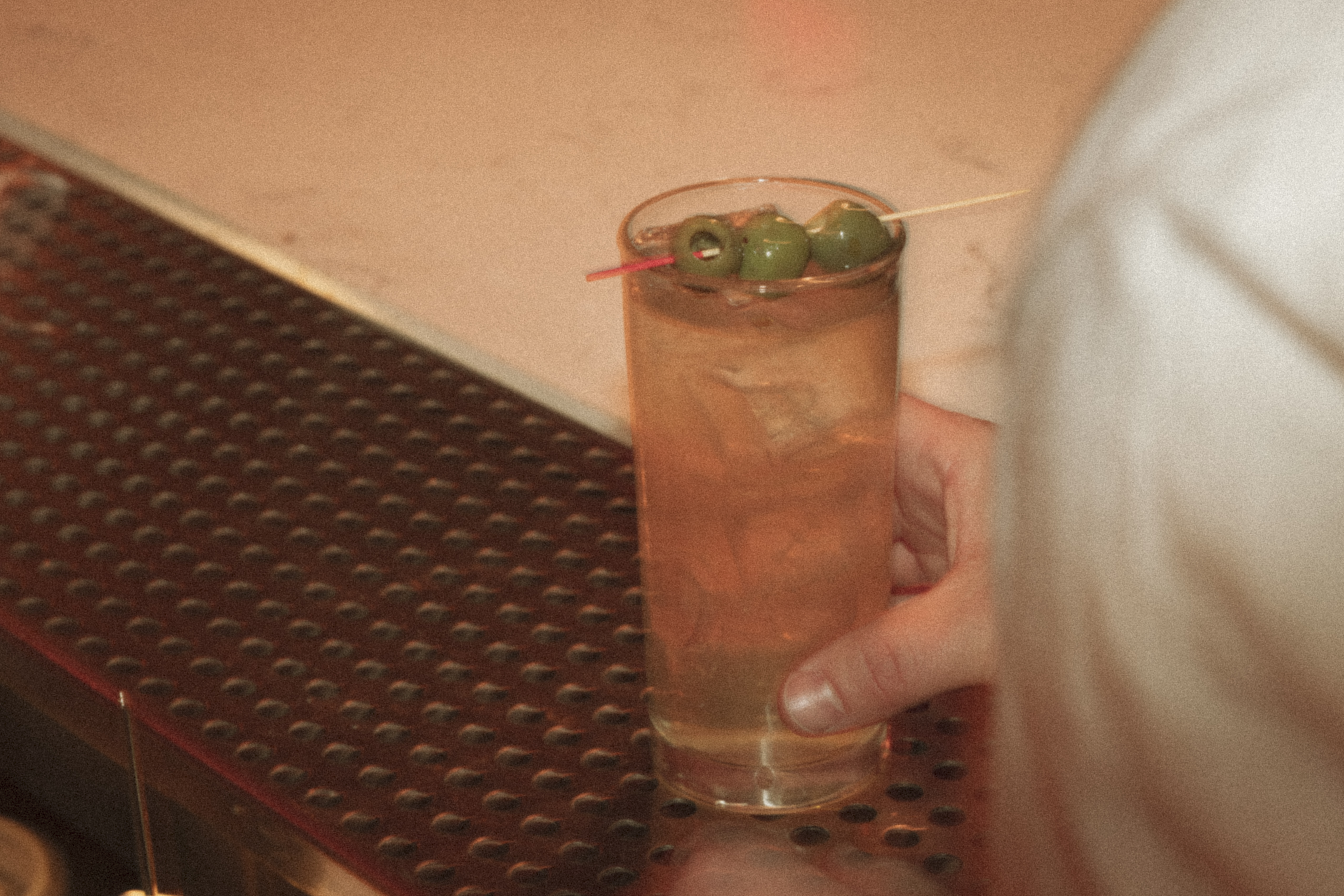 a person holding a glass of liquid with olives