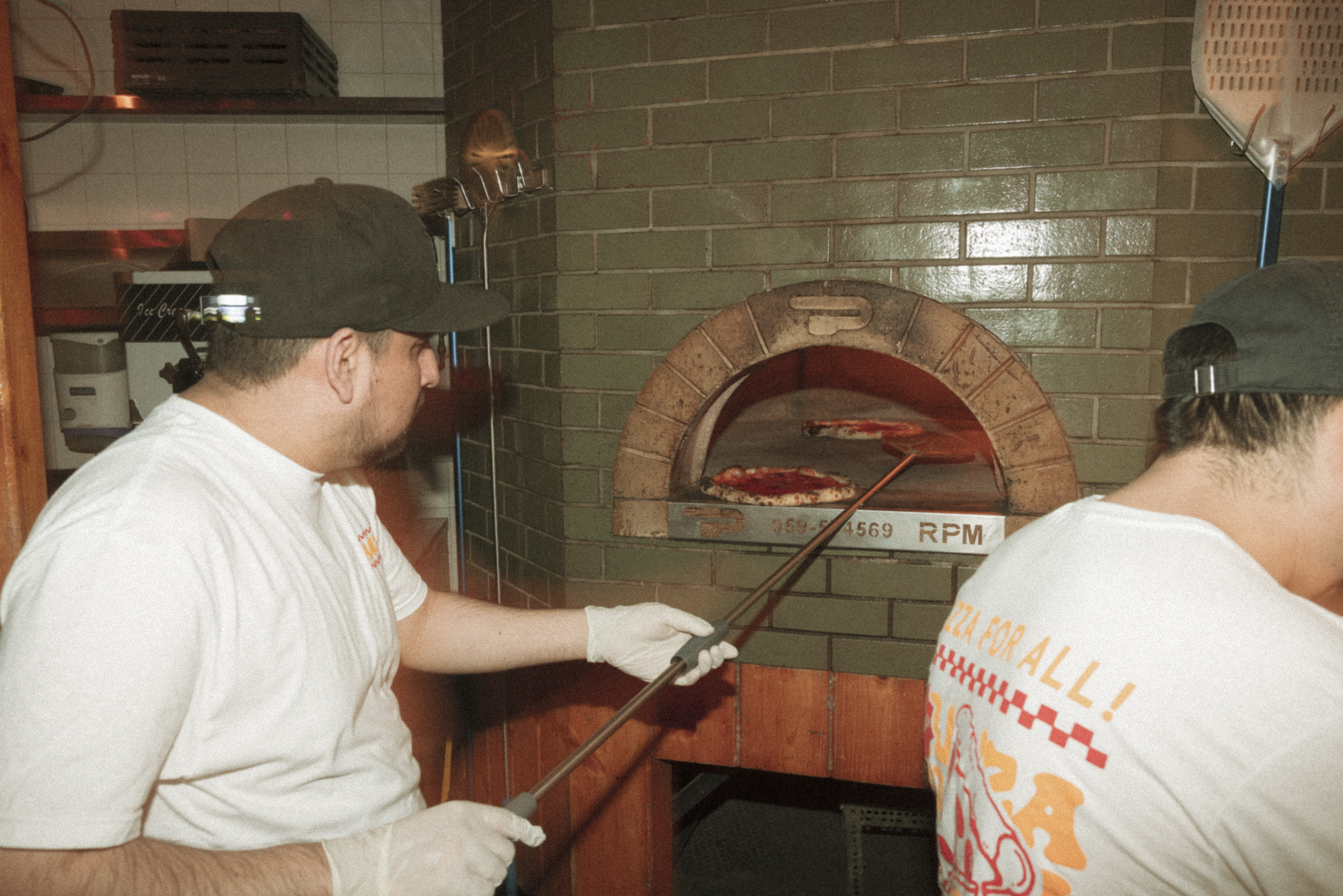a man holding a stick to a pizza in a brick oven
