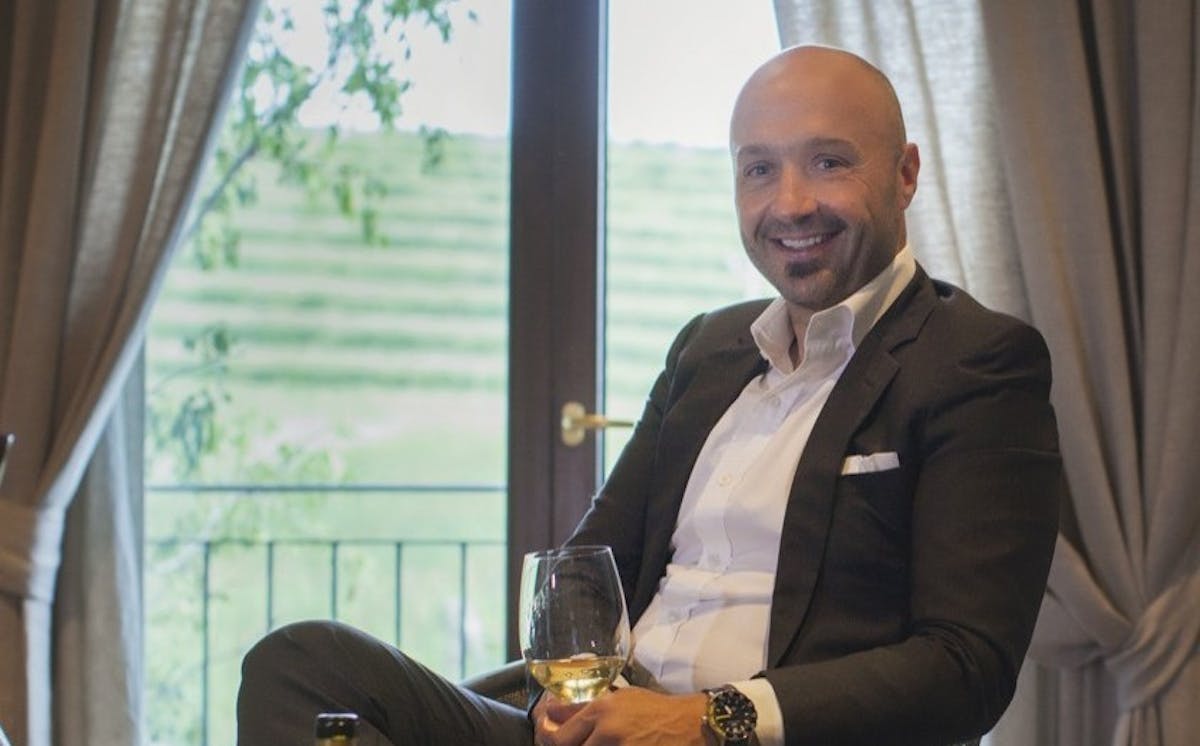 Joe Bastianich wearing a suit and tie sitting in front of a window
