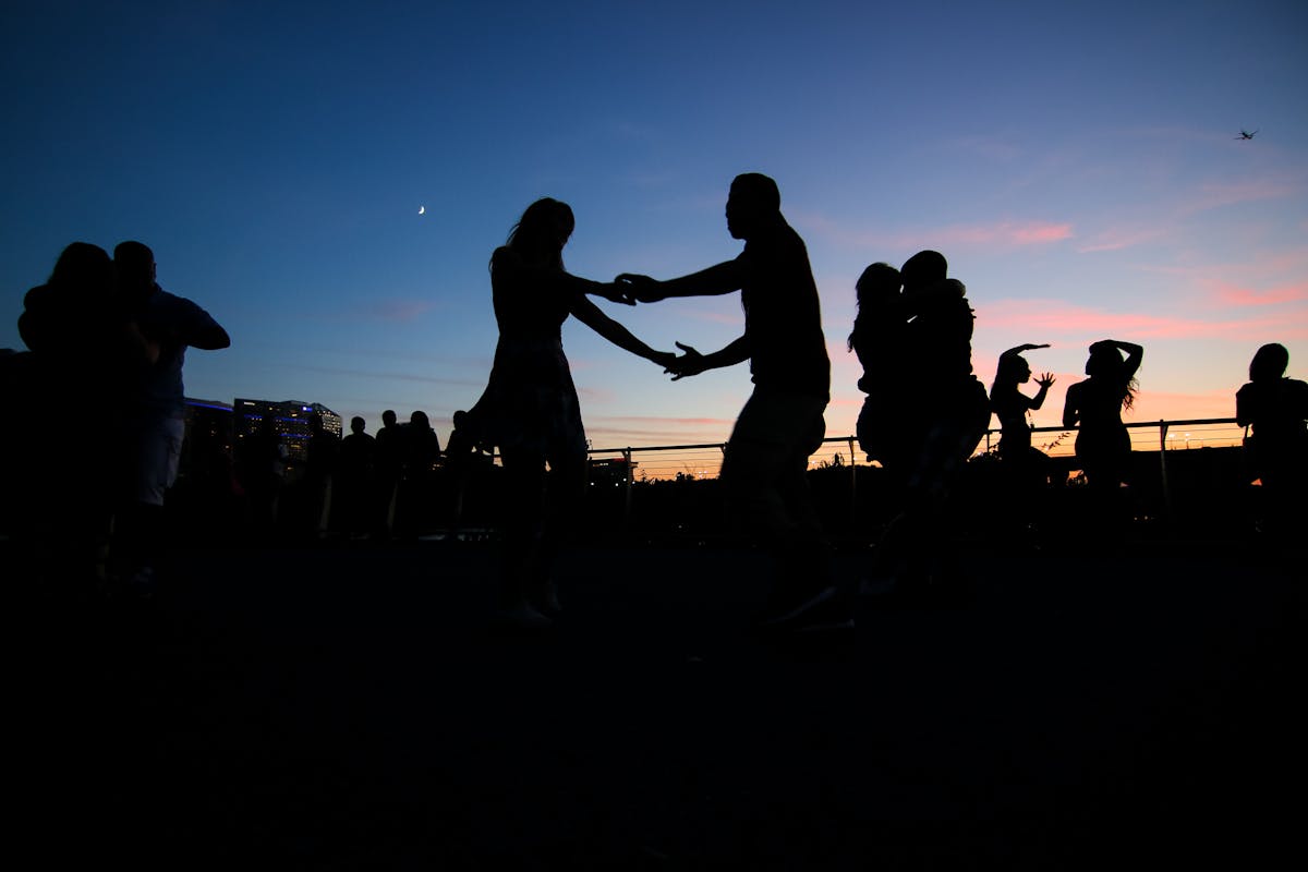 Silhouettes of people salsa dancing on a rooftop during sunset