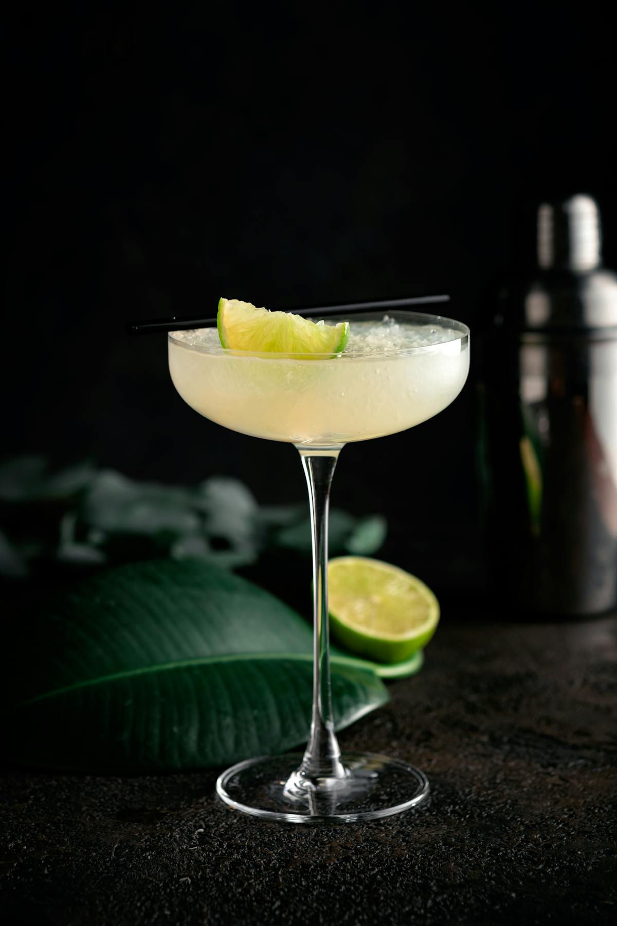 Class lemon cocktail in martini glass against black background with a shaker