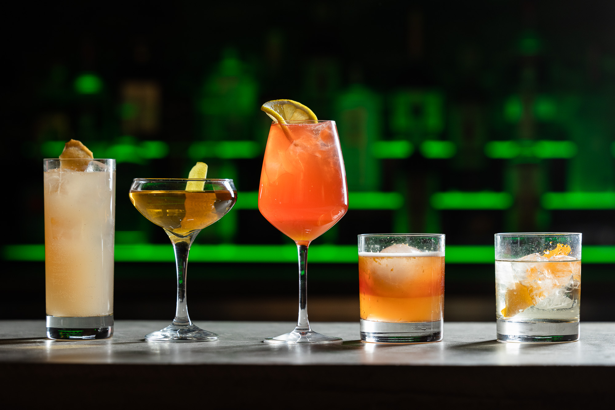 Cocktails on the bar in all different cocktail glassware. Cocktails range in size and color.