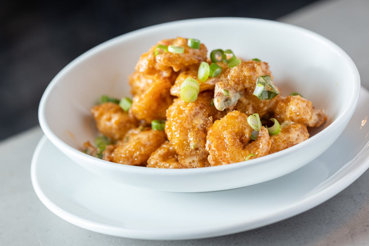 Bang Bang Shrimp in a white bowl, topped with green onion 