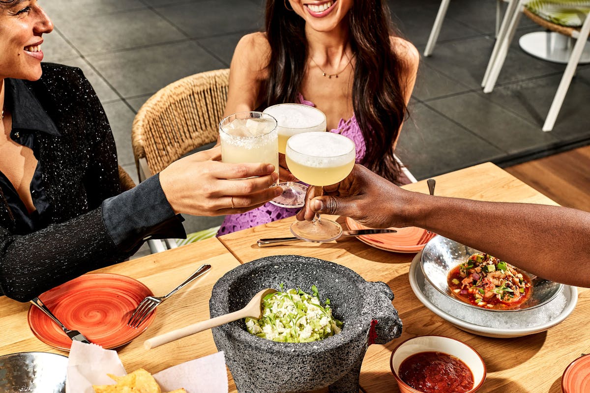 three people sitting at a table with plates of food and cocktails