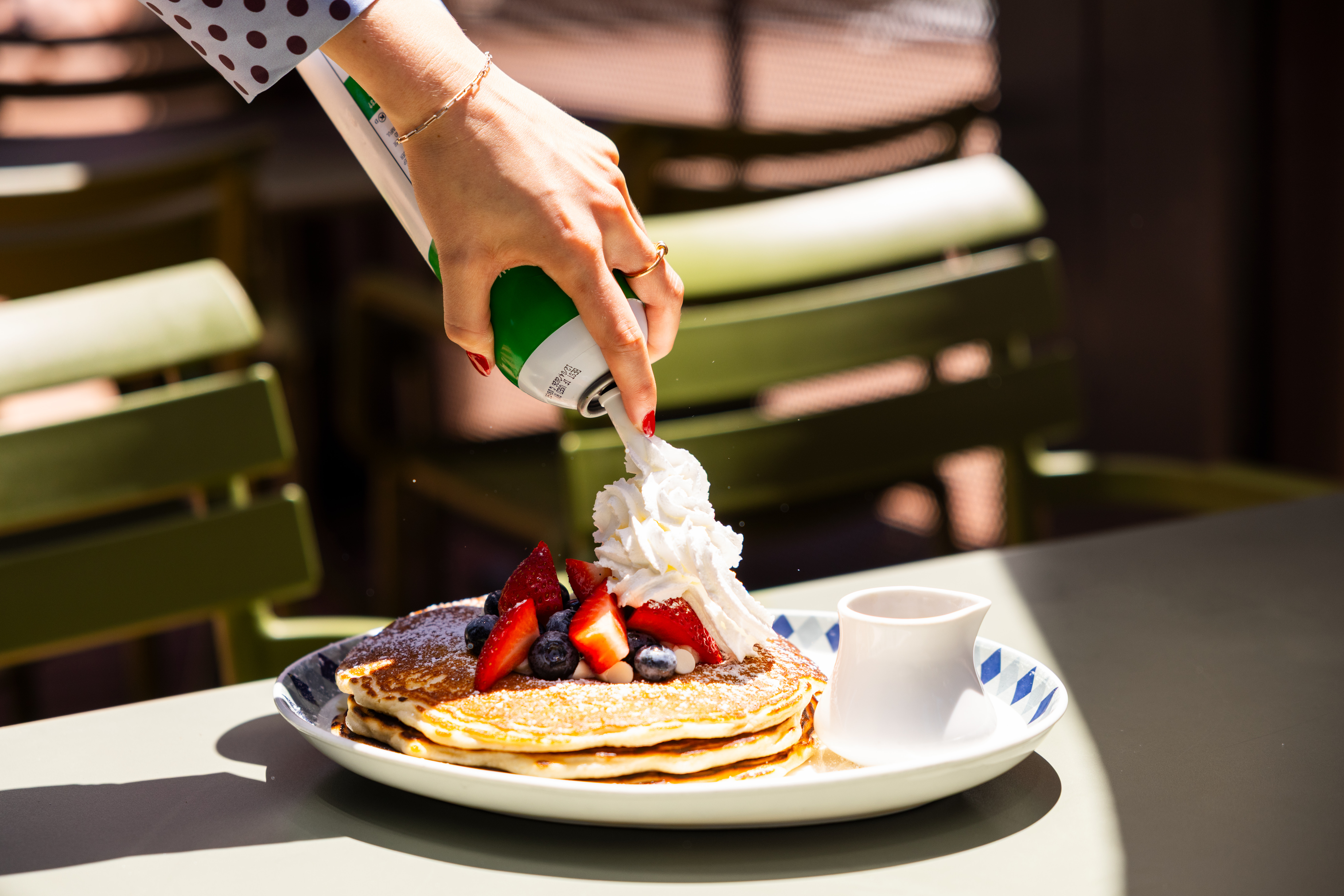 a person spraying whipped cream onto a plate of pancakes