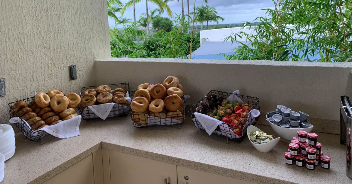 A brunch station with baskets of assorted bagels, pastries, jams, cream cheese cups, and butter arranged outdoors by Potions In Motion.