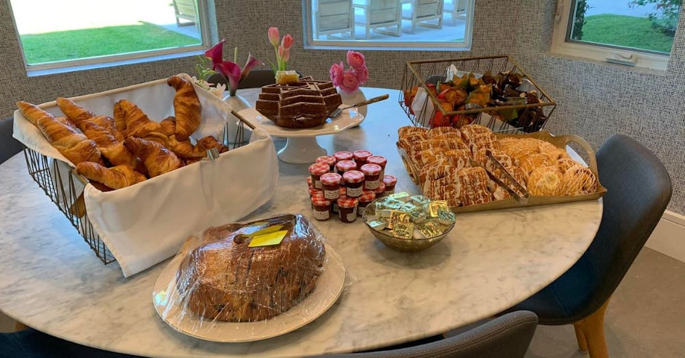 A breakfast spread featuring croissants, pastries, muffins, jams, and a cake arranged on a round marble table for a Potions In Motion brunch setup.
