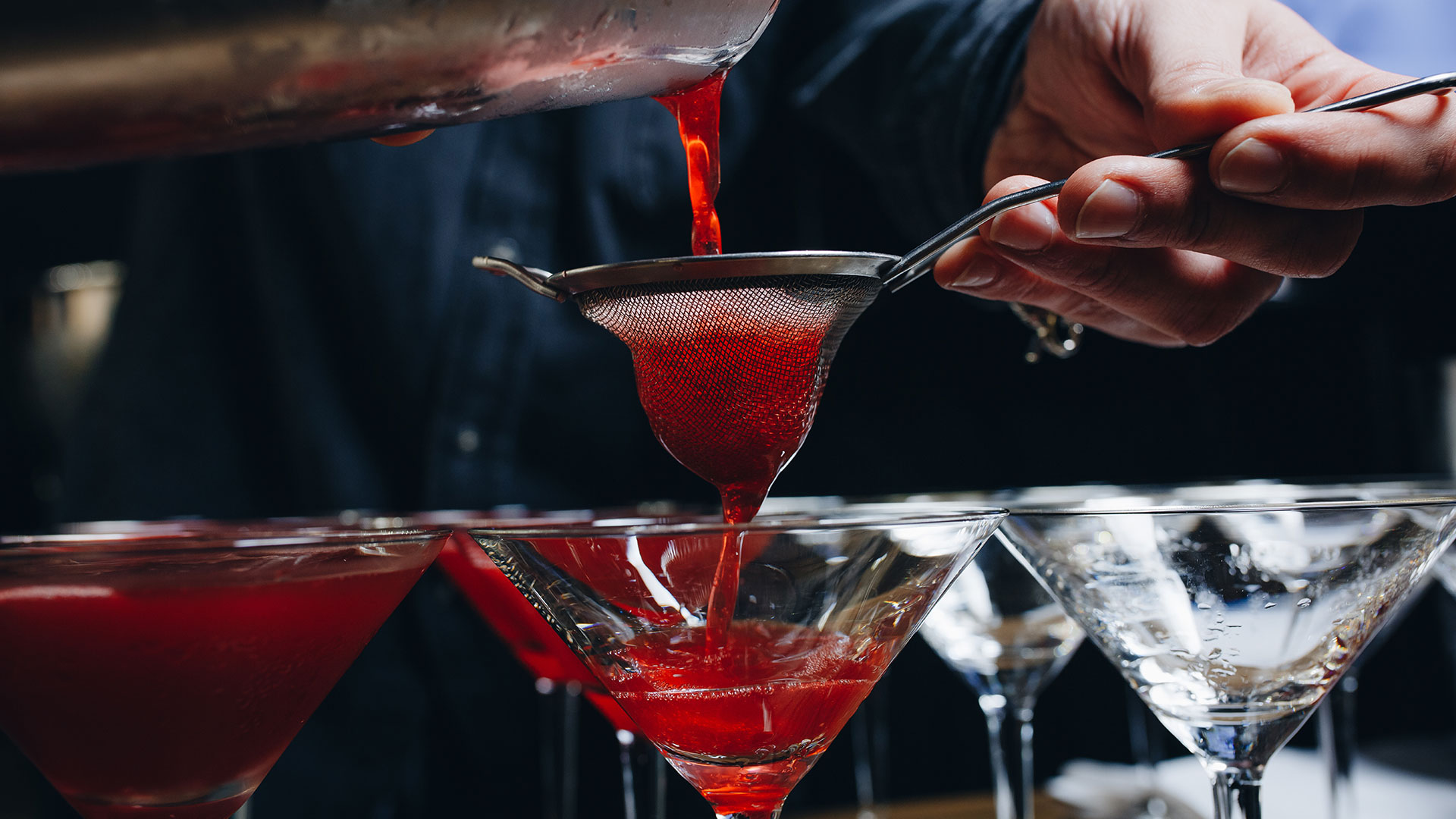 Bartender pouring red cocktail into martini glasses during cocktail party catering event