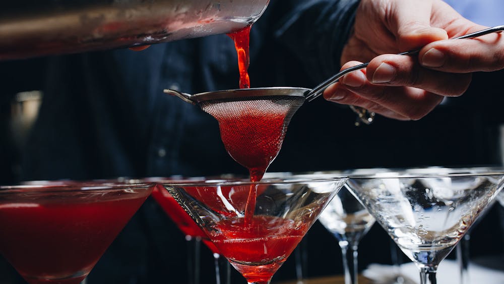 Bartender pouring red cocktail into martini glasses during cocktail party catering event