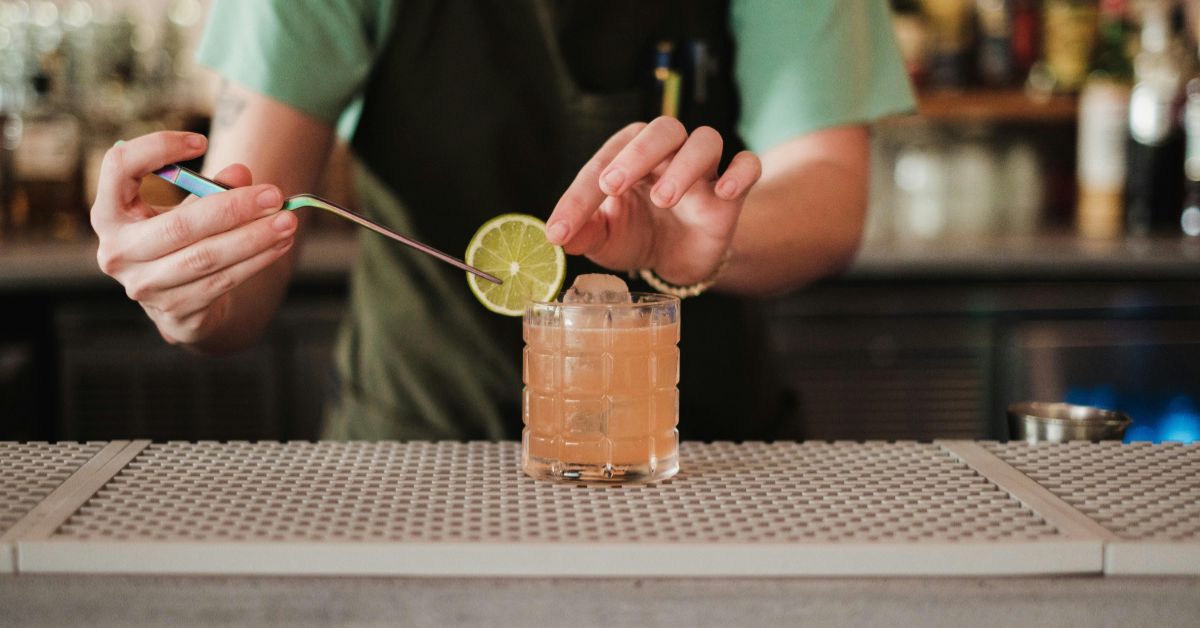 A bartender using professional bar tweezers to precisely place a fresh lime wheel onto a refreshing pink grapefruit cocktail