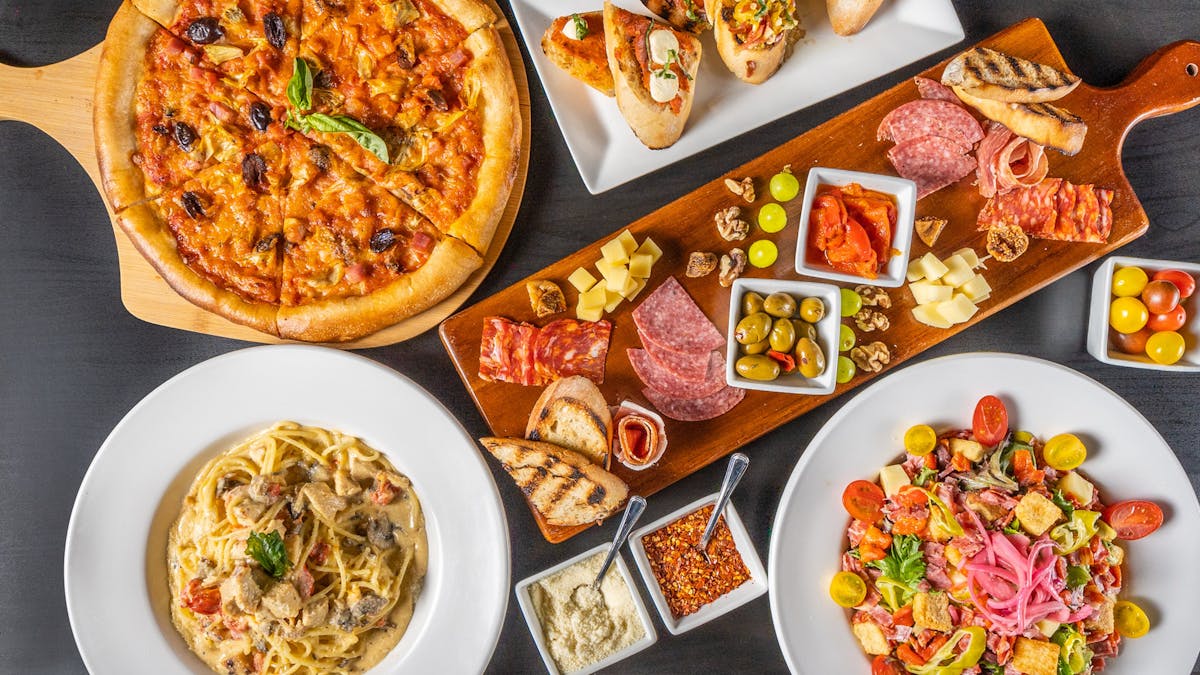table filled with pizza, pasta, and italian dishes