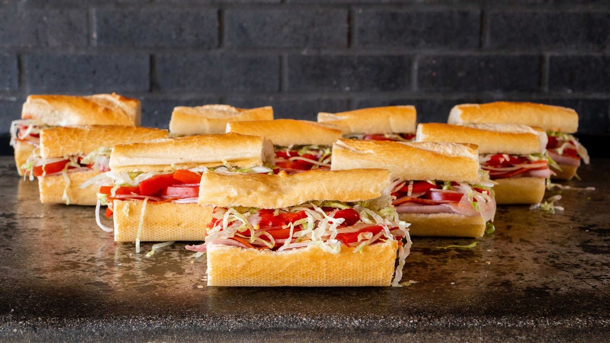 Assorted Fat Sal’s catering sandwiches with deli meats, shredded lettuce, and tomato on hoagie rolls