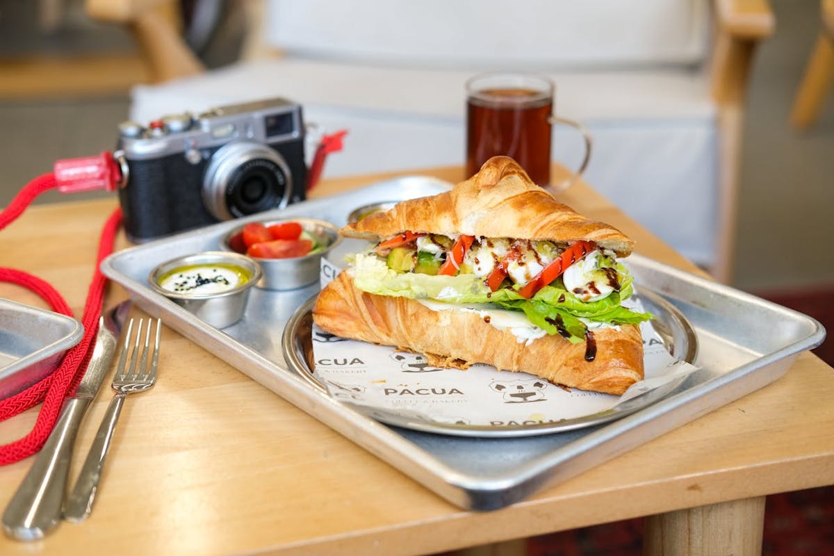 A regional turkey sandwich served on a flaky croissant with fresh vegetables, plated in a casual café setting.