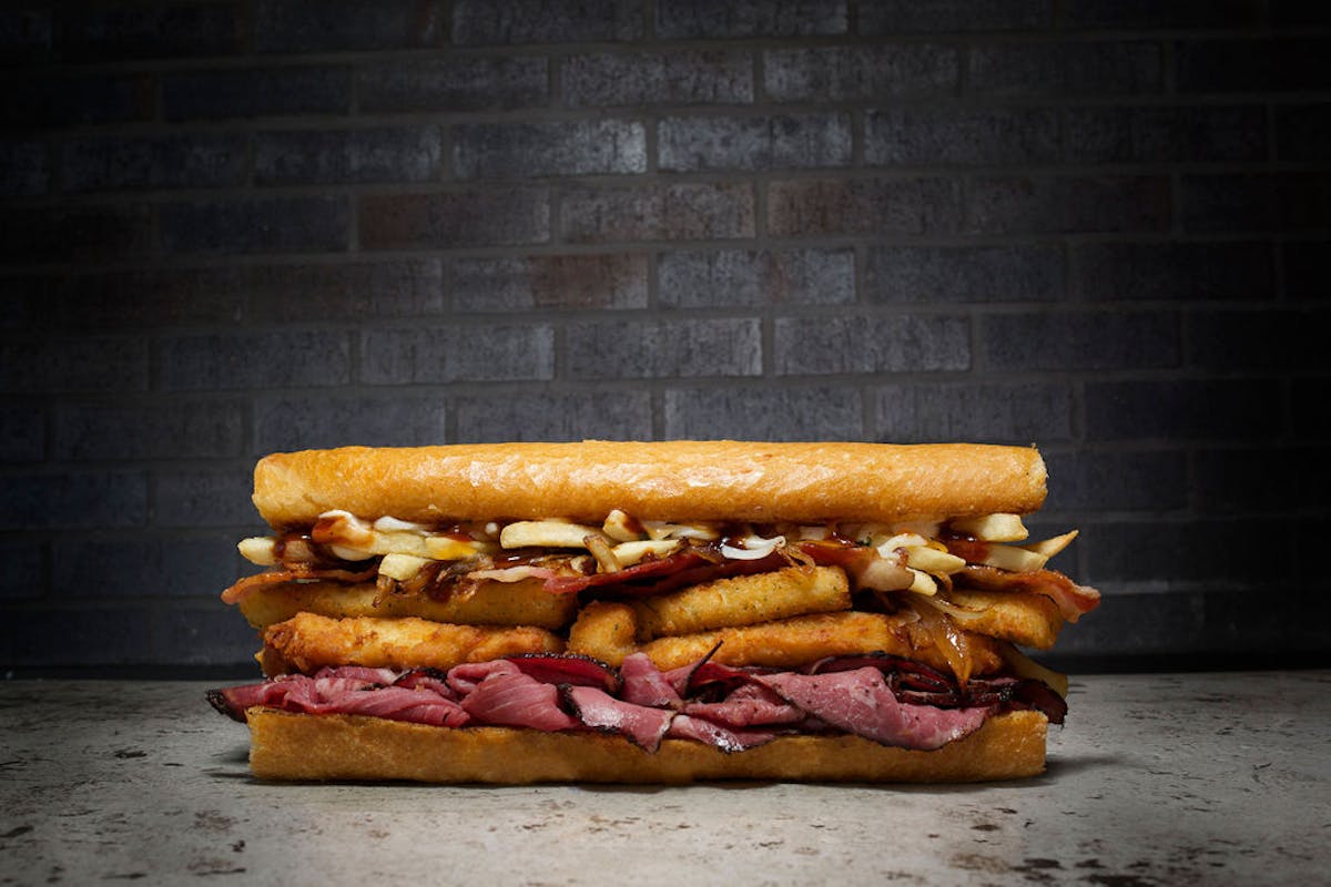 Overstuffed Italian sub sandwich with roast beef, mozzarella sticks, fries, and BBQ sauce on a hero roll from Fat Sal’s.