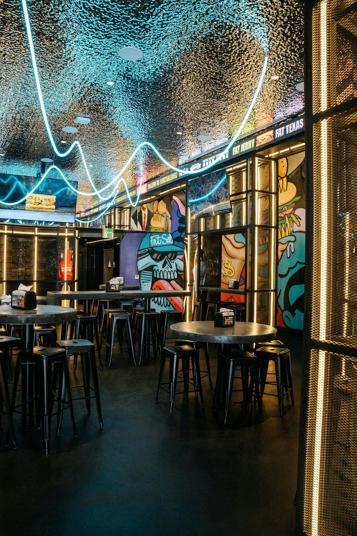 Interior of Fat Sal’s Glendale location featuring neon lighting, street-art style murals, and modern industrial seating