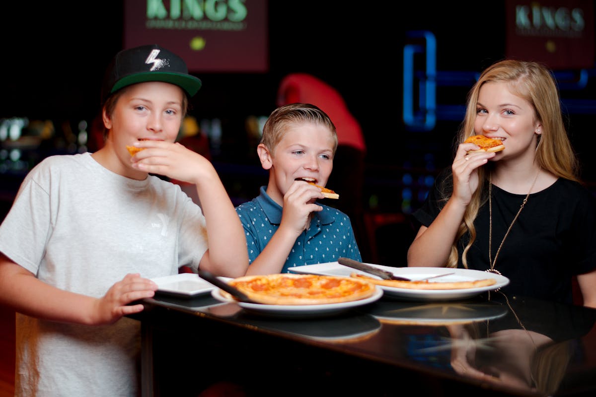 a young boy eating a slice of pizza sitting on top of a table