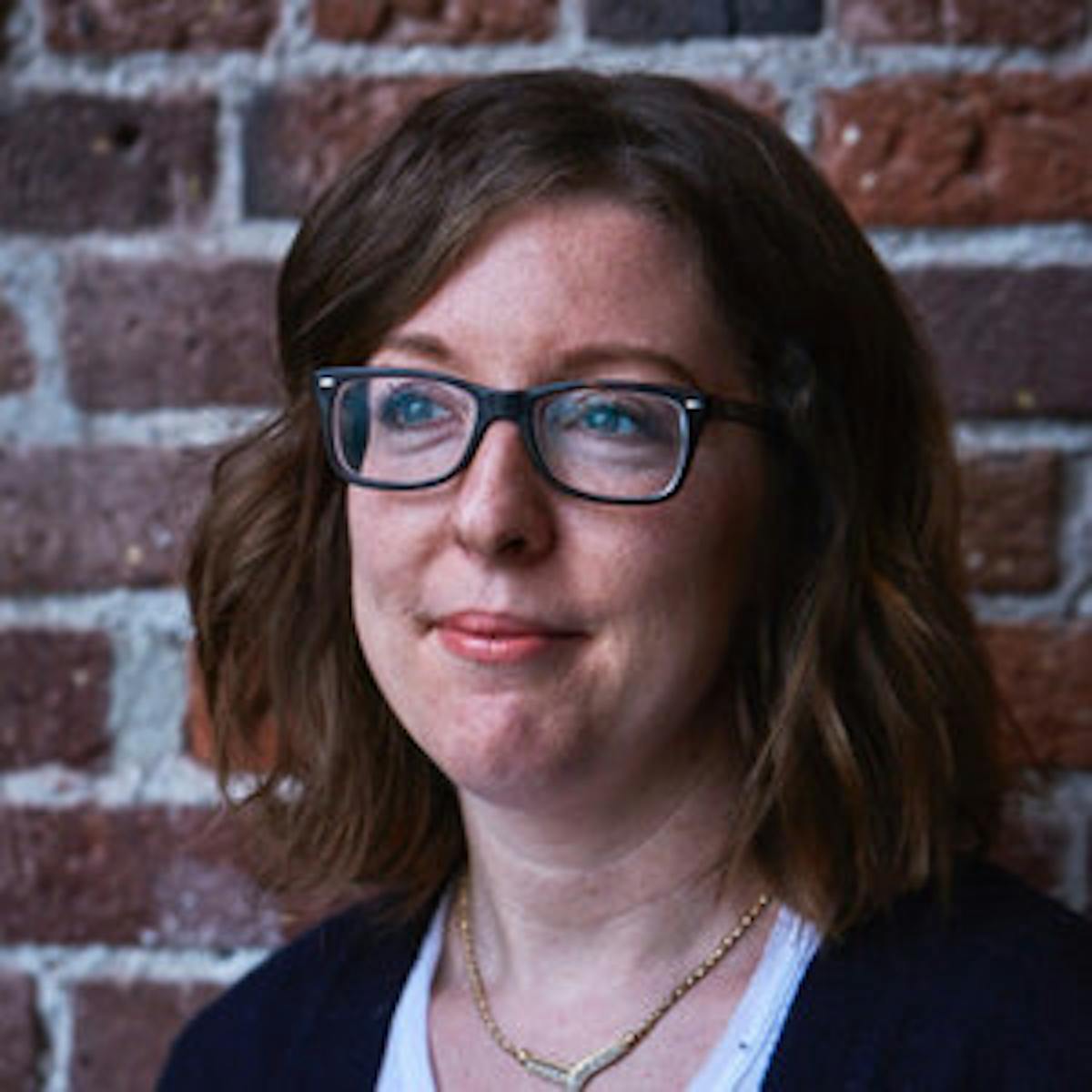 a person wearing glasses and standing in front of a brick building