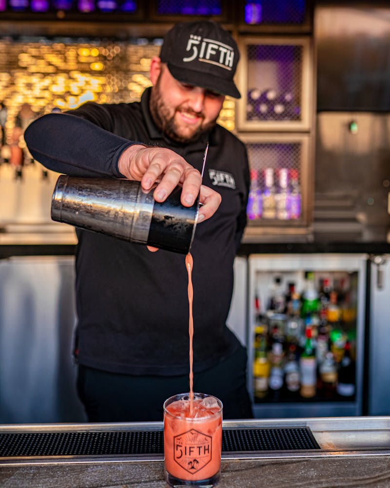 Jason from The FIFTH pouring a red cocktail into a FIFTH cocktail glass. 