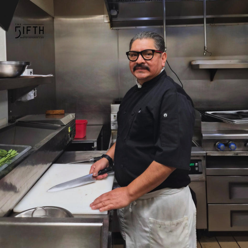 a man in a black shirt and white apron standing in a kitchen