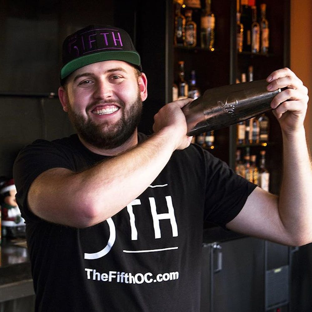 a man wearing a FIFTH shirt and FIFTH hat shaking a cocktail shaker