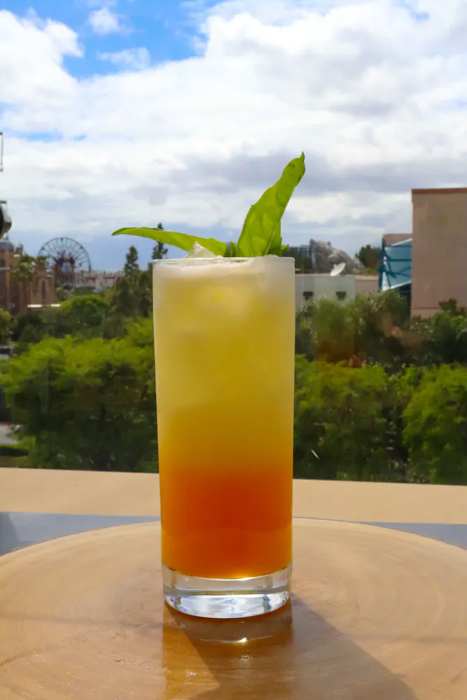 a tall, multicolored cocktail with a leaf garnish
