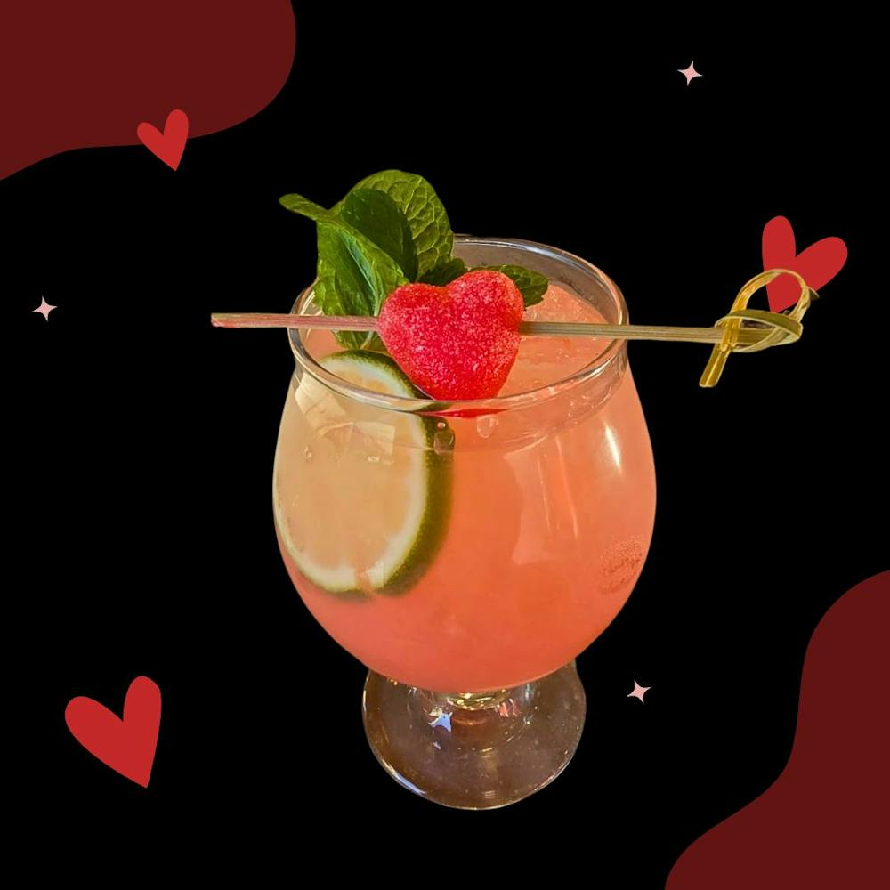 a glass of pink cocktail featuring heart candy garnish.