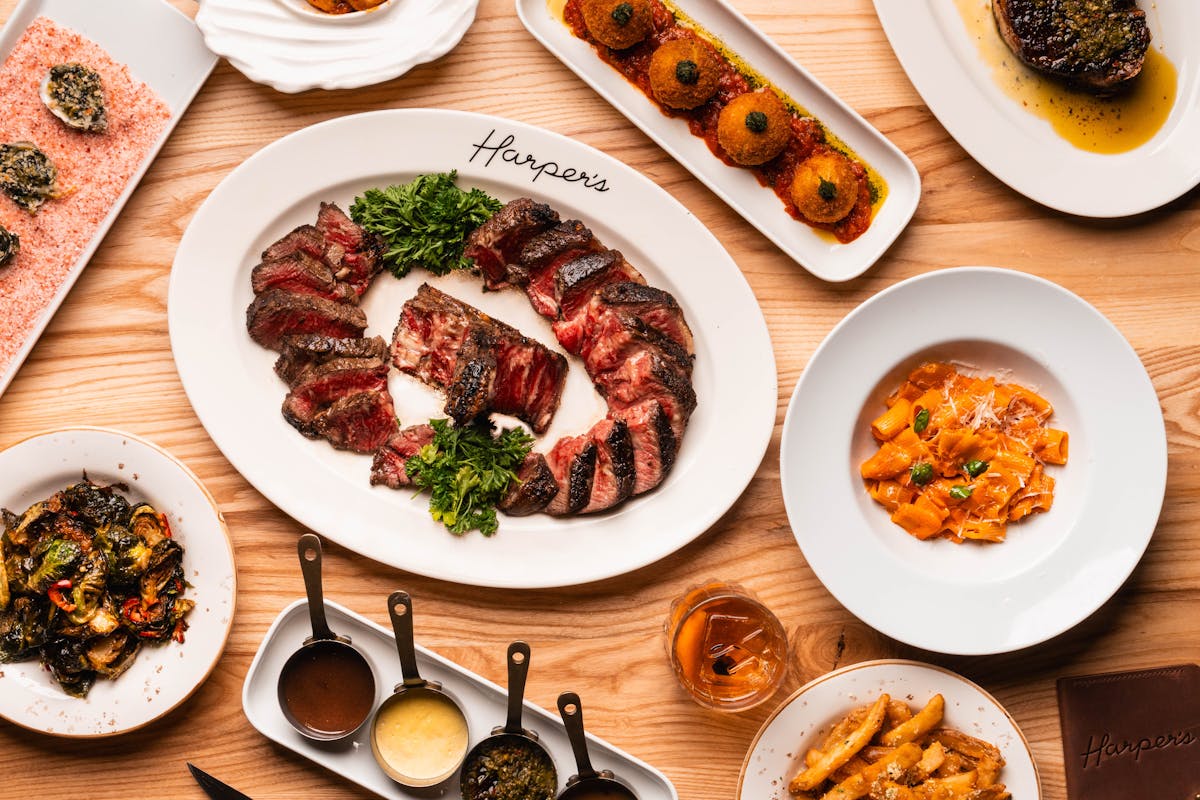 Porterhouse steak, signature sauces, and appetizers on Harper's Steakhouse table.